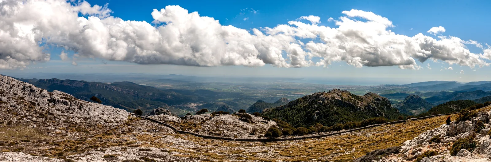 Limestone ridges of the Serra de Tramuntana under cumulus cloud, with the plain and the sea beyond.