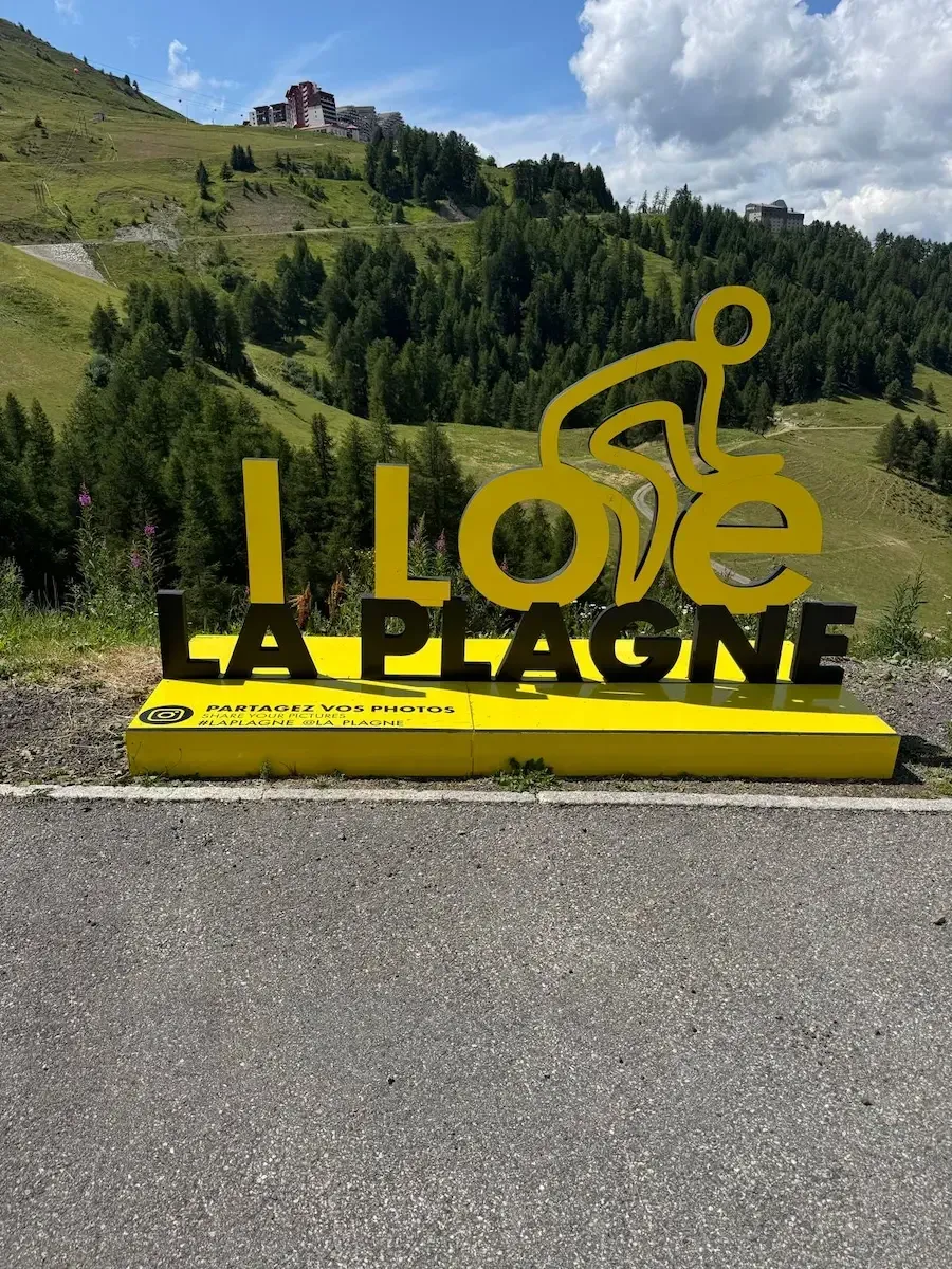 Rennradfahrer am gelben „I ❤ LA PLAGNE"-Tour-de-France-Denkmal am Gipfel der Montée de La Plagne