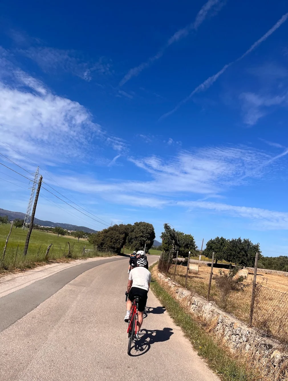 Cyclist on a quiet country road in Mallorca — clear blue skies and the Serra de Tramuntana mountains in the distance