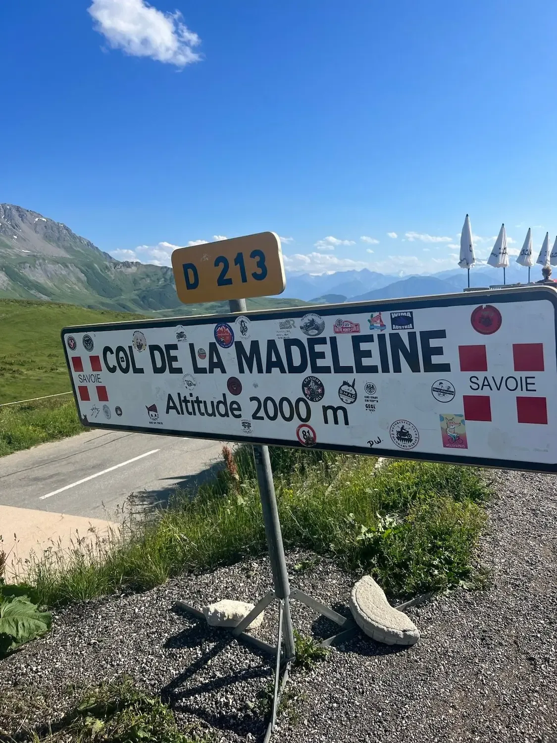 The stickered D213 summit sign at 2,000 m, parasols of the refuge behind.