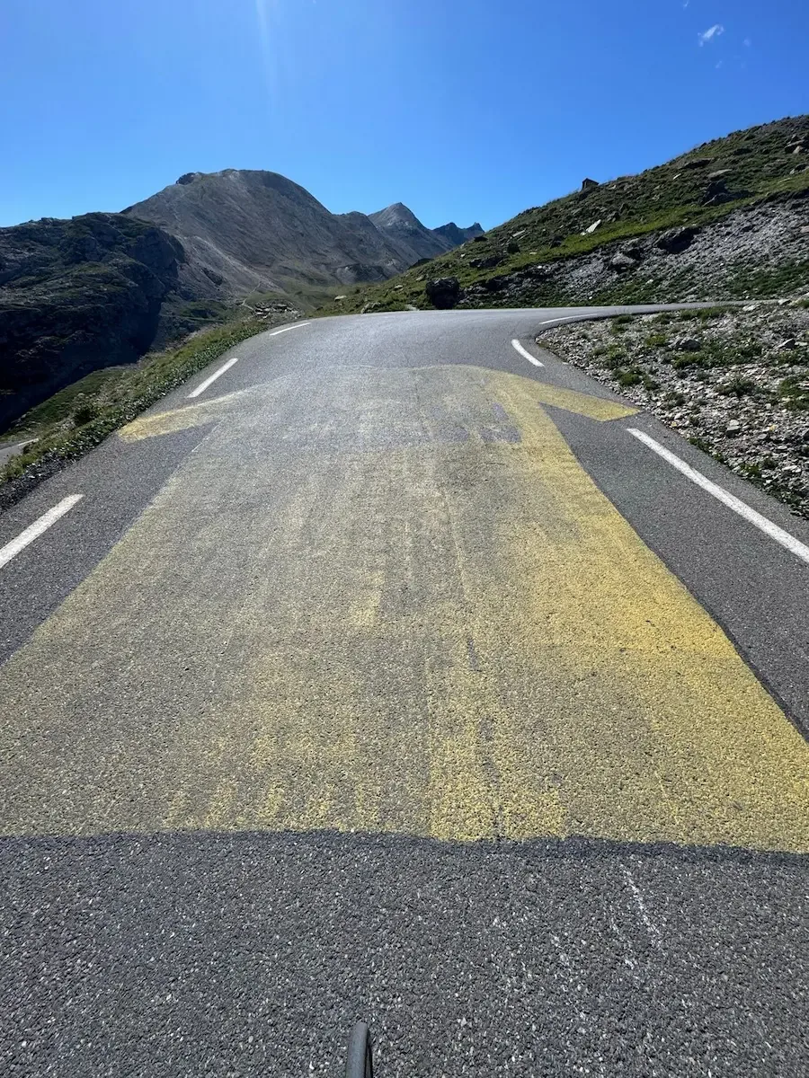 Faded yellow Tour arrows on the tarmac, peaks ahead