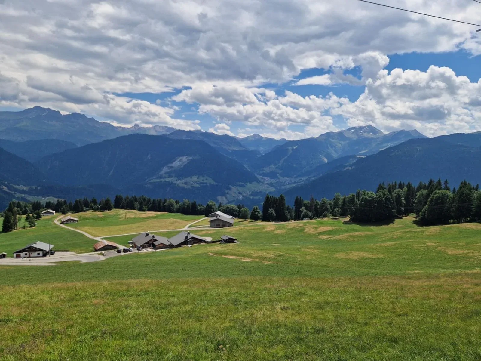 Green Beaufortain pastures with layered peaks fading under streaked cloud