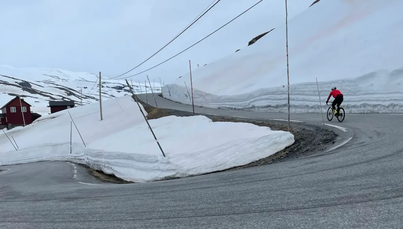 Rennradfahrer auf der Sognefjellsvegen zwischen Schneewänden – Route Lom – Sognefjellshytta, Jotunheimen, Norwegen