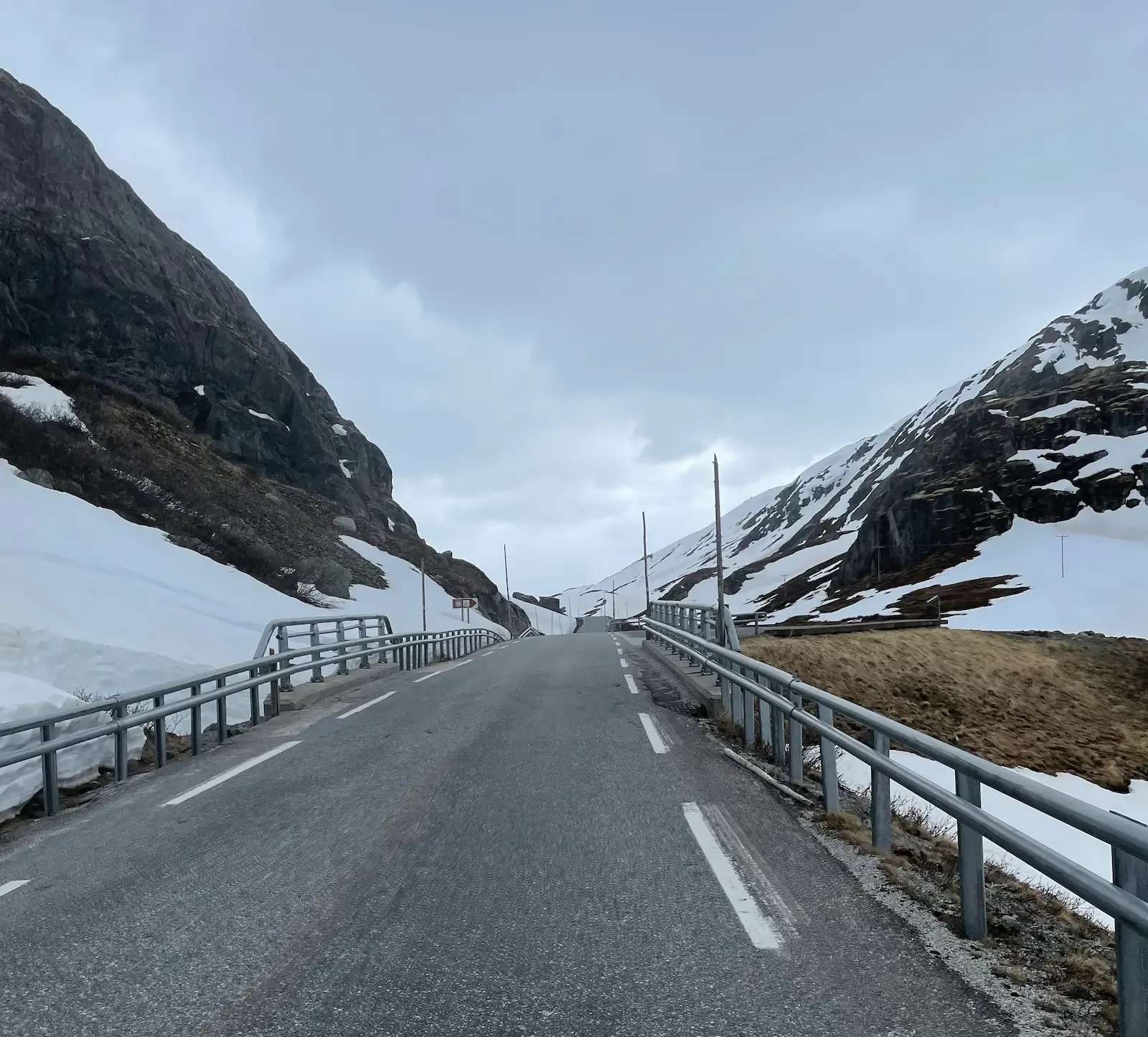 Bridge between rocky, snow-patched slopes under a heavy grey sky.