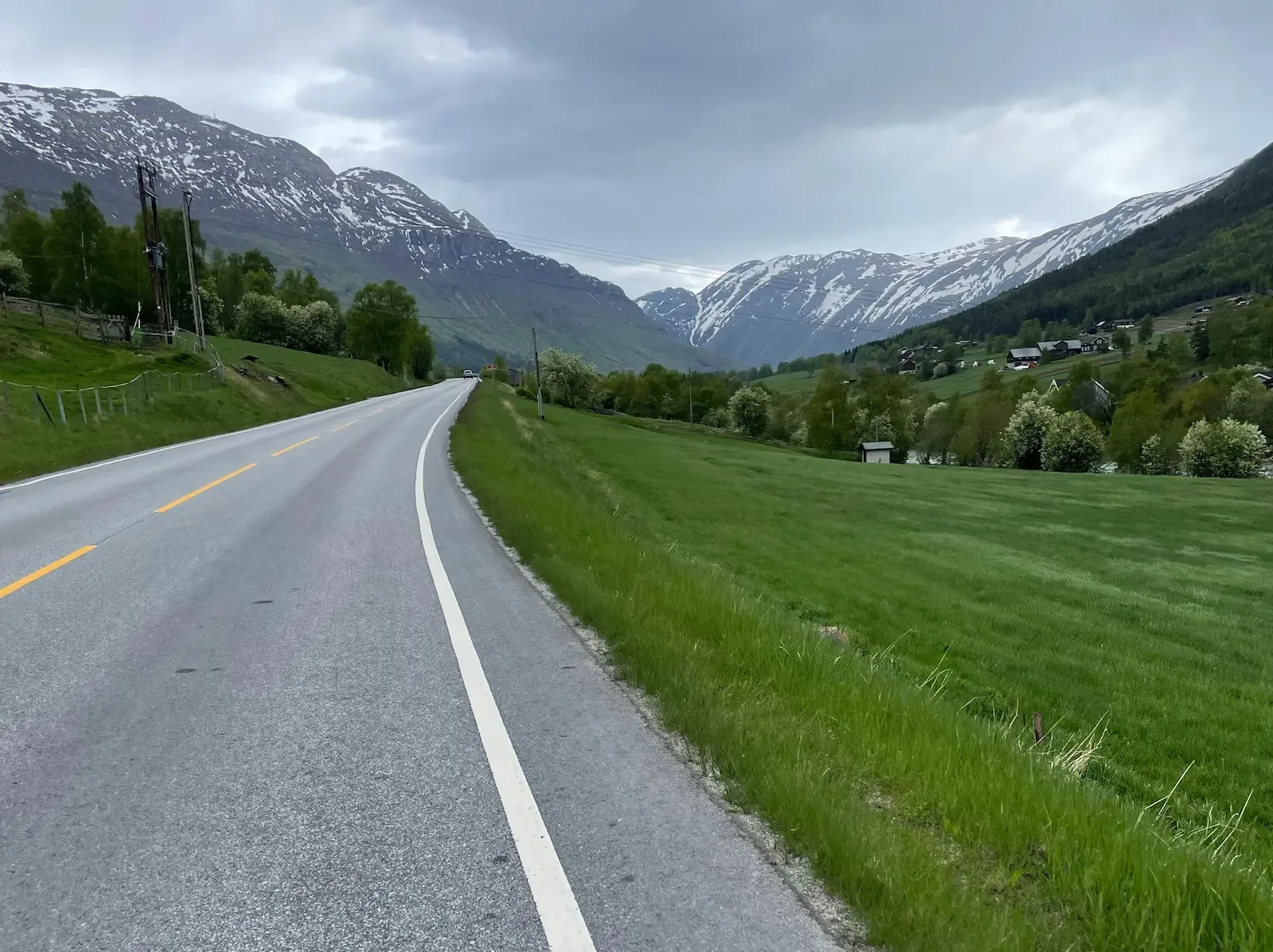 Valley road through green meadows toward the snow-capped wall of Jotunheimen.