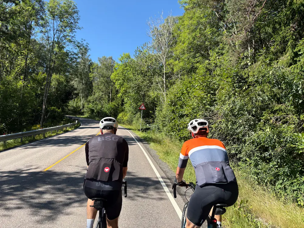 Dos ciclistas al pie de Rundvollbakken, con bosque cerrado a ambos lados
