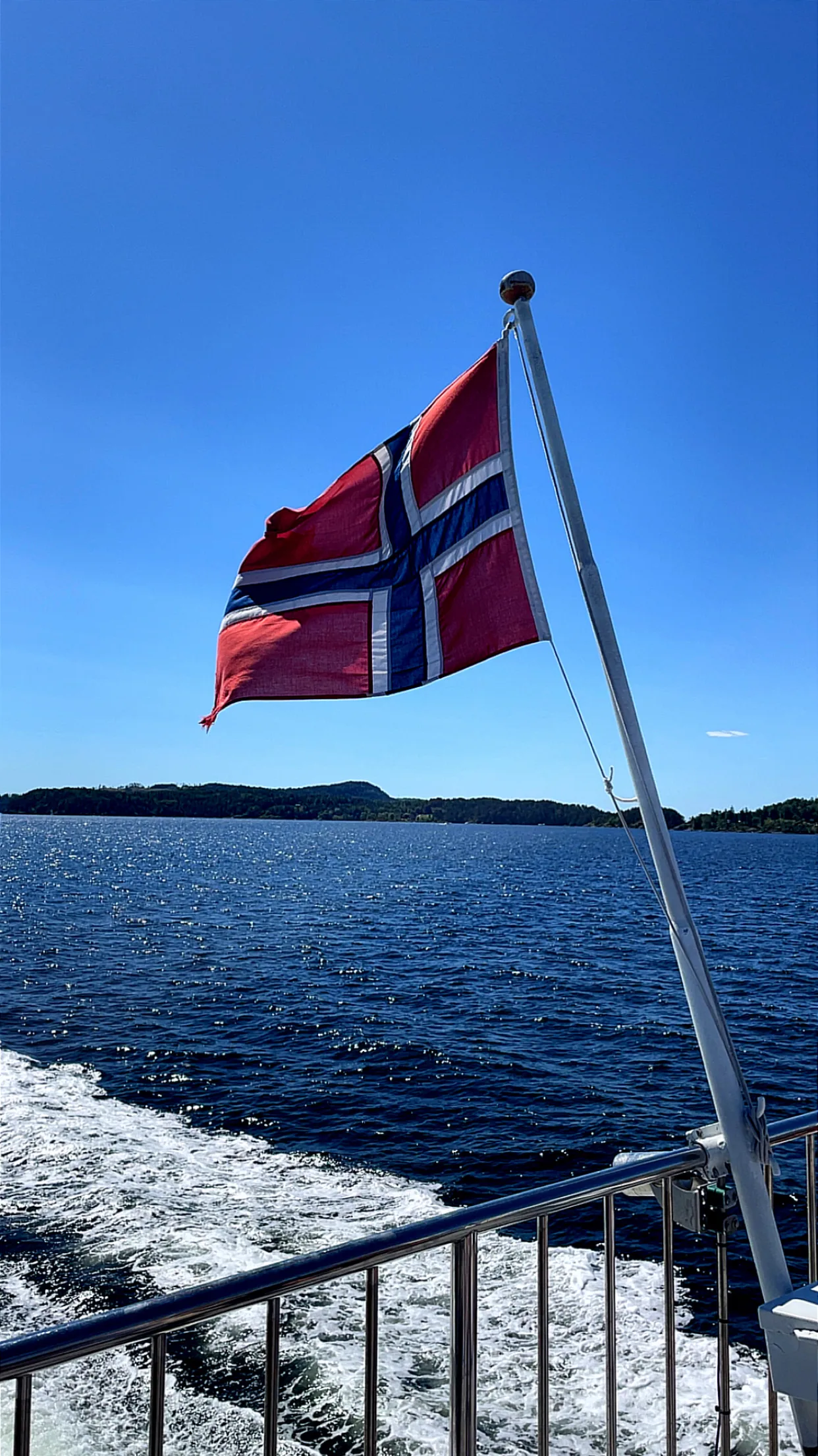 La bandera noruega ondea en la estela del ferry, con Hurum en el horizonte.
