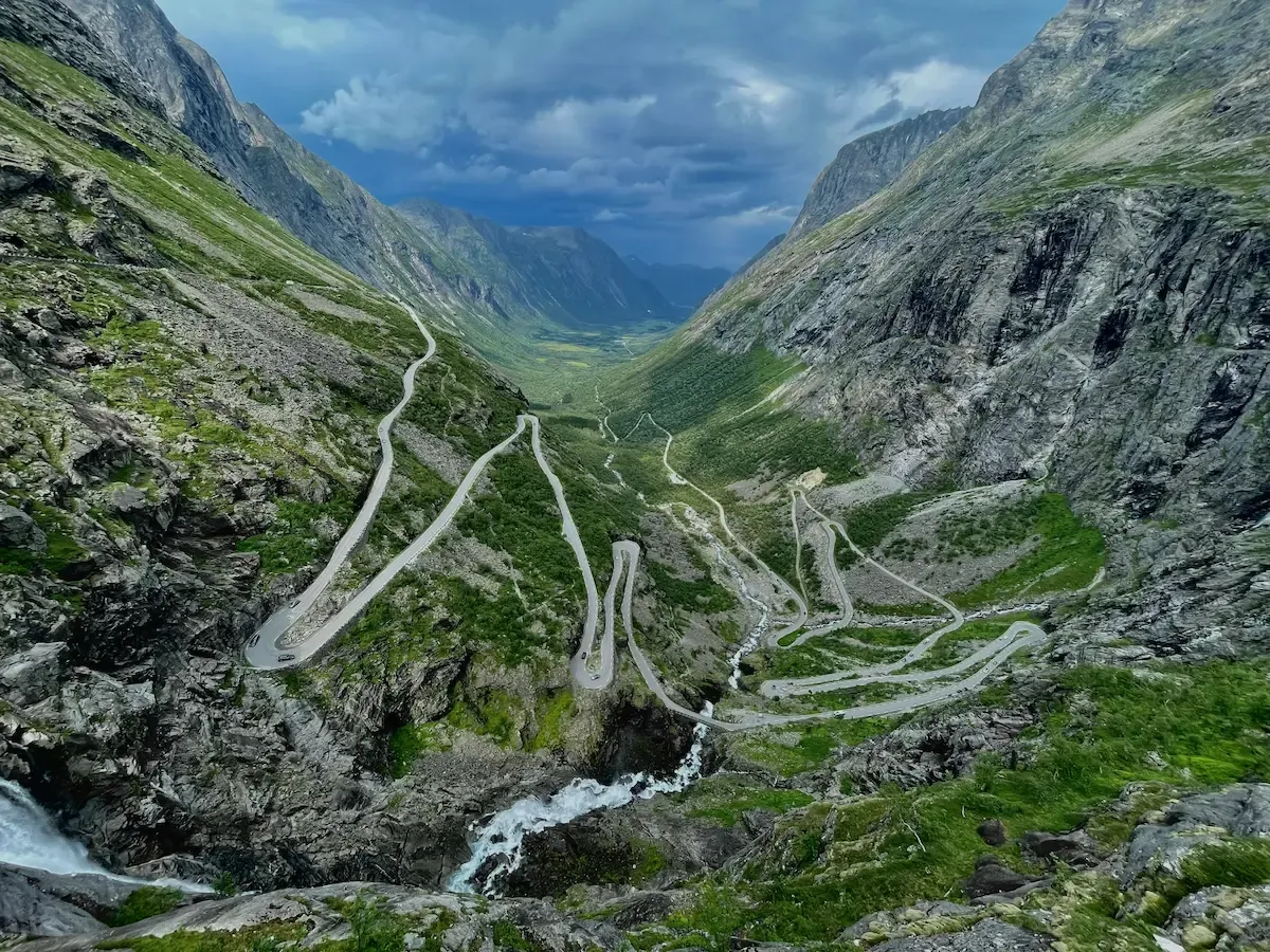 Trollstigen's eleven hairpins seen from above, with Stigfossen tumbling alongside the road and the peaks of Bispen and Kongen on either side.